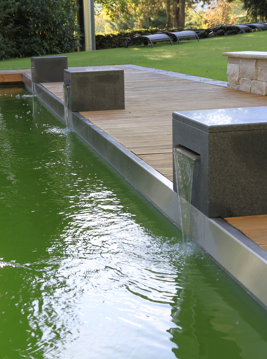 Naturschwimmbad mit Wasserfontänen aus dunkelgrauem Naturstein