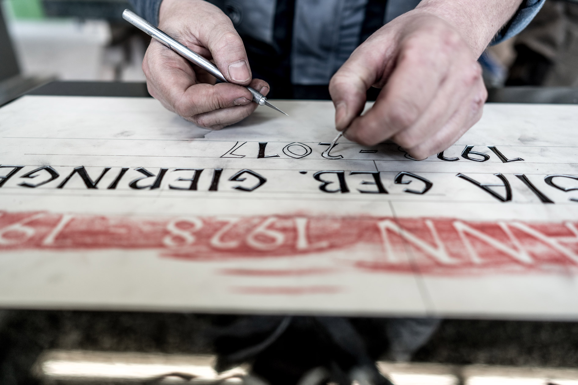 Nahaufnahme der Hände eines Steinmetzes, der an der Inschrift eines Grabsteins arbeitet